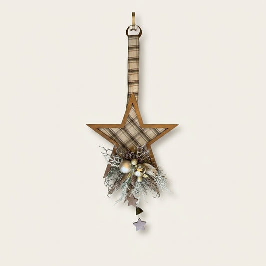 A rustic wooden star-shaped hanging ornament decorated with a beige and brown plaid fabric center, a hanging loop at the top, and a decorative cluster at the bottom featuring faux pine branches, small white berries, and dangling star charms.