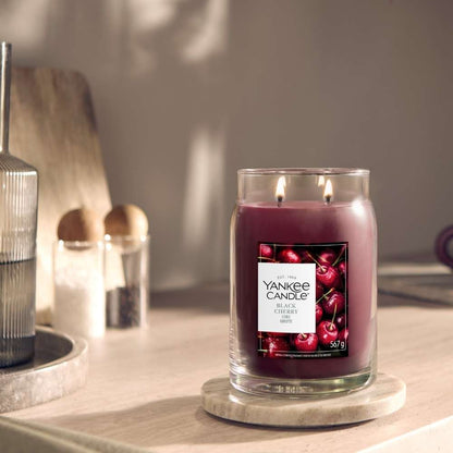 A Yankee Candle All Over Cherry scented candle in a clear glass jar with two wicks, sitting on a round marble coaster on a wooden table in a softly lit room.
