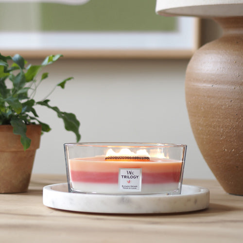 WoodWick Blooming Orchard Trilogy candle in a clear glass jar with an open lid against decorative background