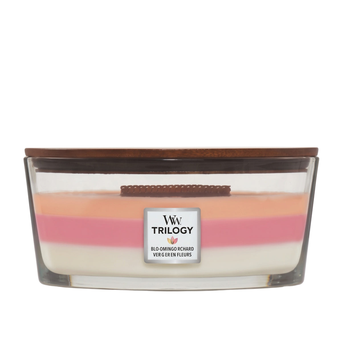 A Trilogy scented candle in a clear glass container with a dark brown wooden lid, featuring three layered wax colors: cream, pink, and peach. The label reads 'W W TRILOGY' and 'BLOOMING RICHARD VERGE EN FLEURS'.