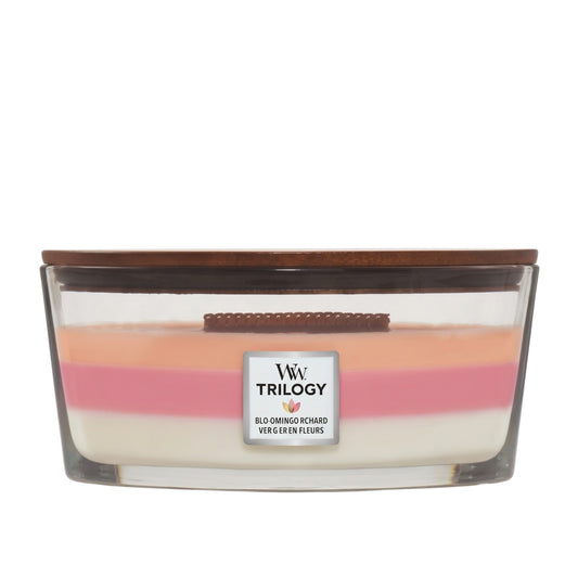 A Trilogy scented candle in a clear glass container with a dark brown wooden lid, featuring three layered wax colors: cream, pink, and peach. The label reads 'W W TRILOGY' and 'BLOOMING RICHARD VERGE EN FLEURS'.