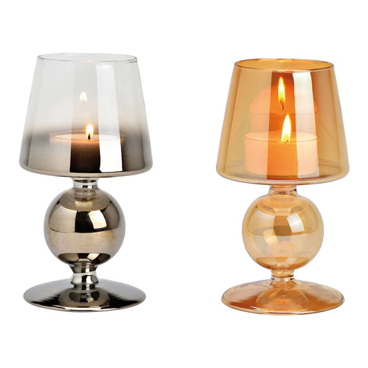 Two goblet-style glass candle holders with lit candles inside, shown in metallic silver and warm amber finishes against a white background.