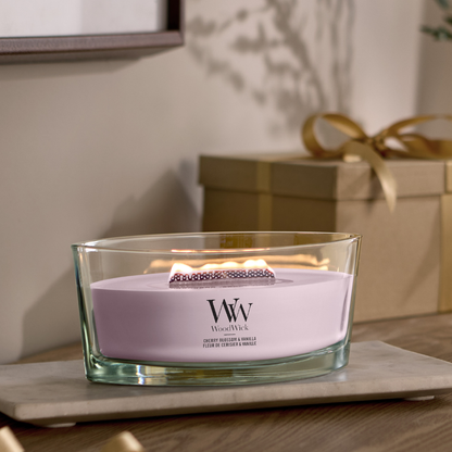 WoodWick Cherry Blossom & Vanilla candle in a clear glass jar with a an open lid against decorative background