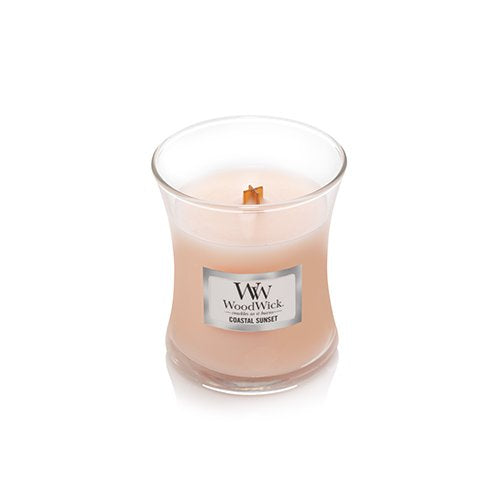 A WoodWick Coastal Sunset scented candle in a clear glass jar with a light peach-pink wax and a single wooden wick, set against a plain white background.