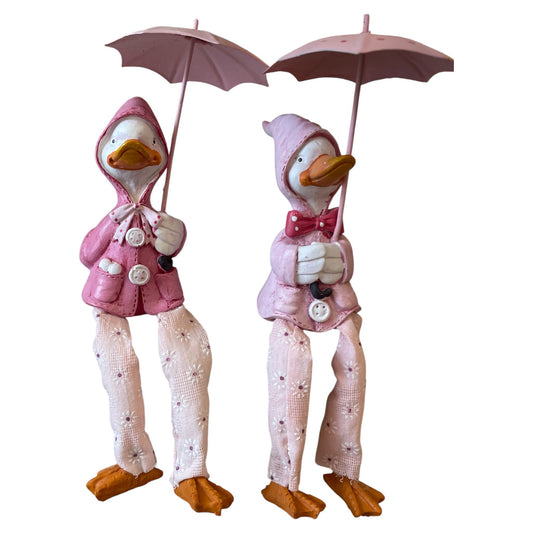 Two decorative ducks in pink outfits holding umbrellas on a white background