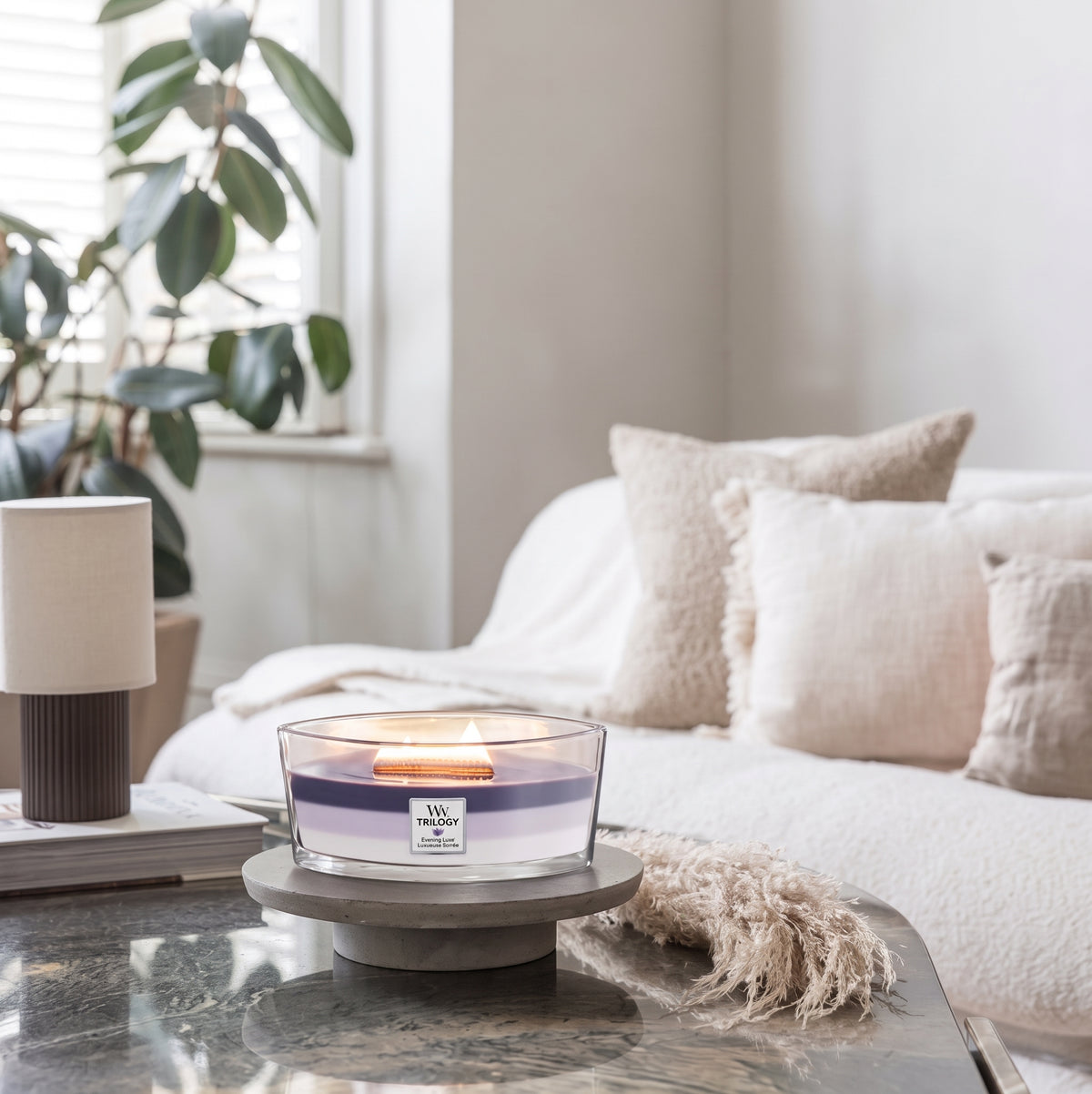 WoodWick Evening Luxe Trilogy ellipse candle in a clear glass jar against decorative backround