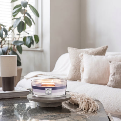 WoodWick Evening Luxe Trilogy ellipse candle in a clear glass jar against decorative backround