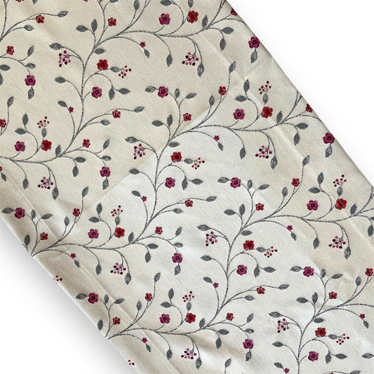 A beige table runner with a floral pattern, featuring various shades of red and gray.