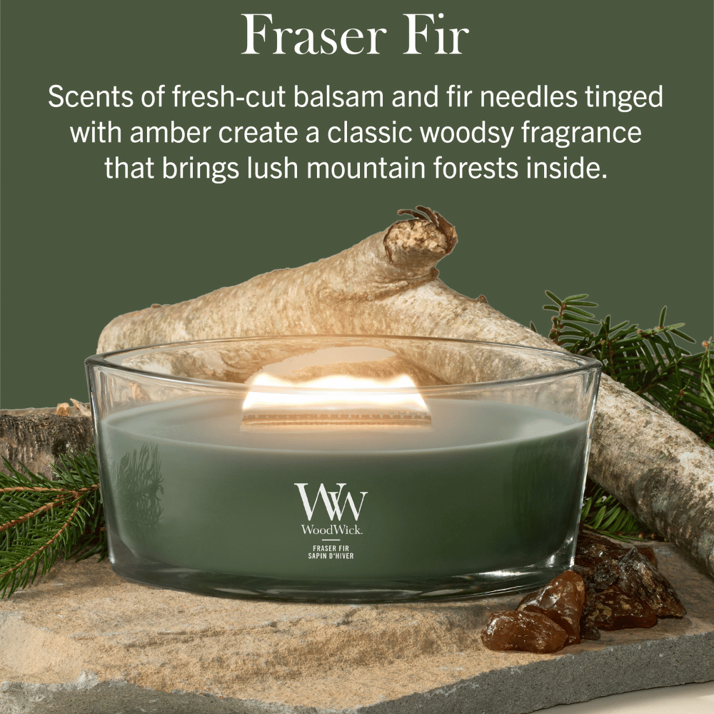 "WoodWick Fraser Fir candle on a stone base surrounded by wood and amber."