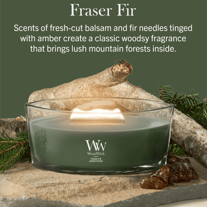 "WoodWick Fraser Fir candle on a stone base surrounded by wood and amber."