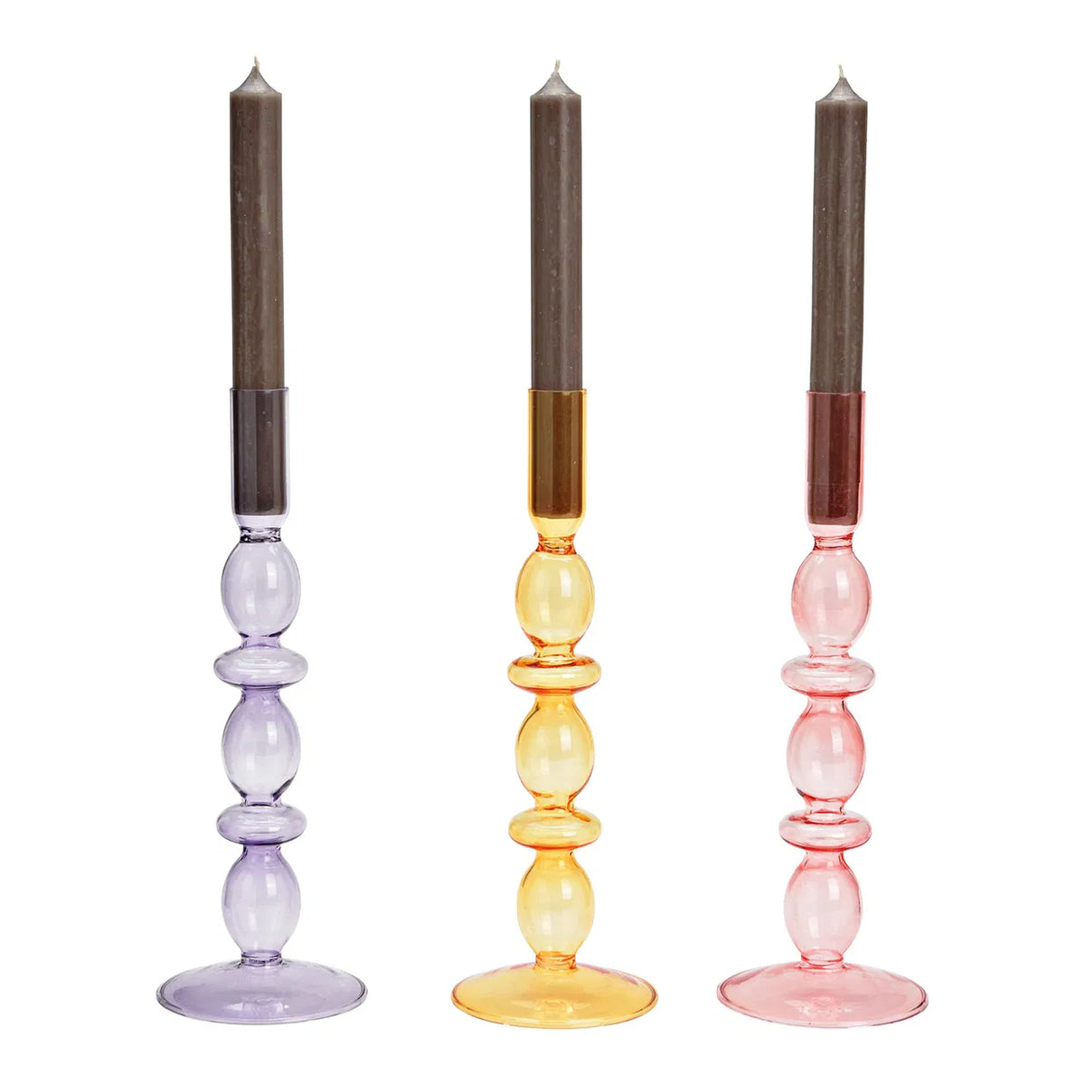 Three glass candle holders in purple, pink, and yellow colors, each with a candle lit in the holder. The holders are placed against a white background.