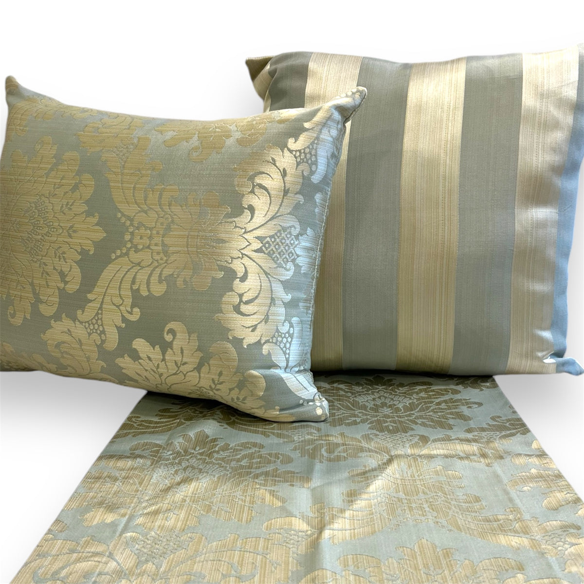 Pair of decorative throw pillows featuring an ornate golden floral damask pattern and soft blue fabric on a golden floral damask pattern ans soft blue runner against a white background.
