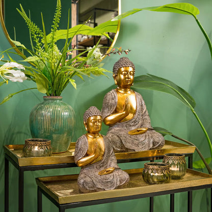 Green glass tealight candle holders displayed on tiered gold accent tables alongside Buddha statues and vibrant green plants.