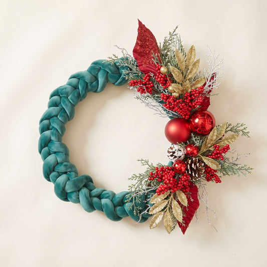 Handmade holiday wreath featuring a teal velvet braided loop decorated with red berries, gold leaves, and pine cones, against a white backgrund