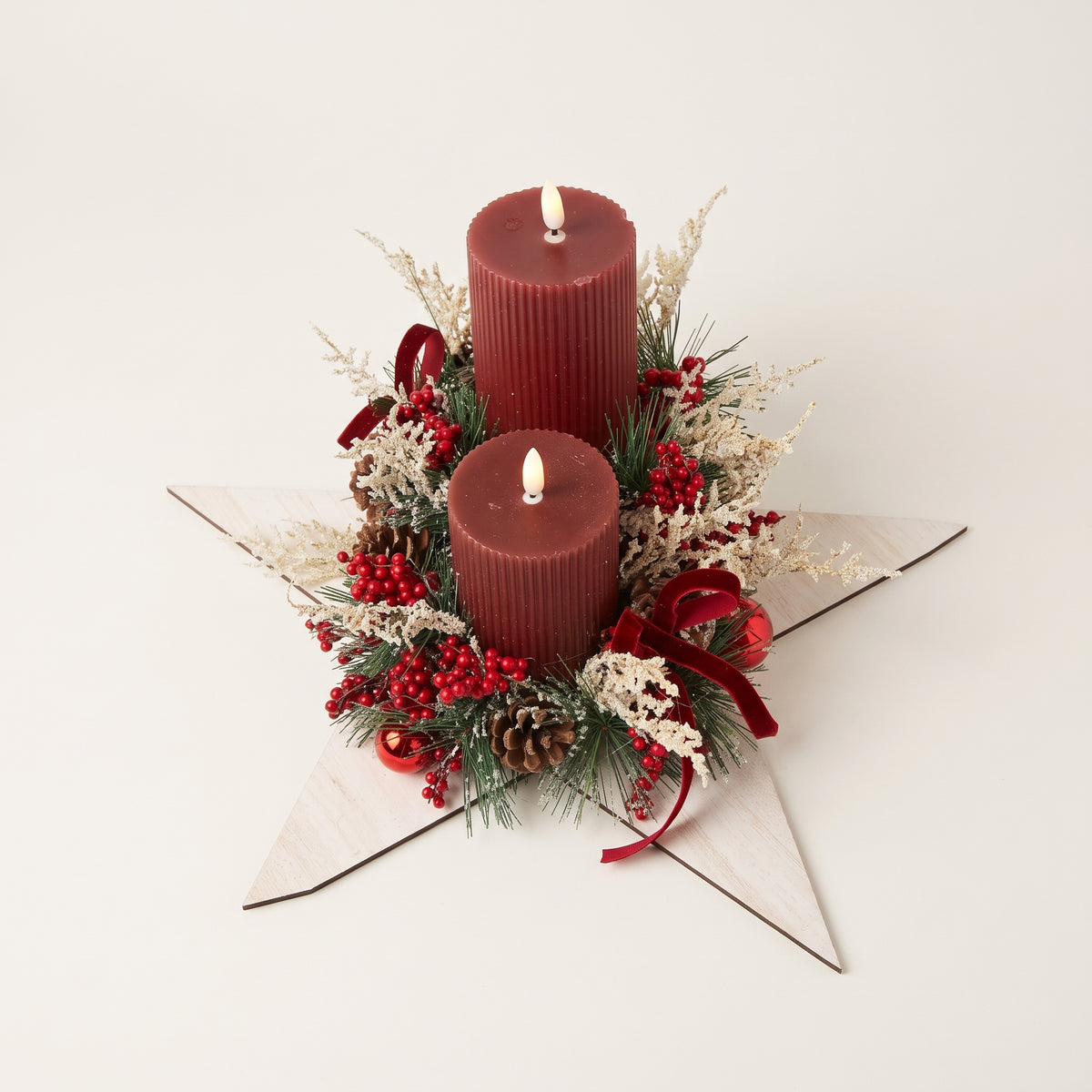 Handcrafted wooden white star candle centerpiece featuring two red pillar candles, natural pinecones, frosted foliage, red decorative balls, and a red velvet bow, against white background