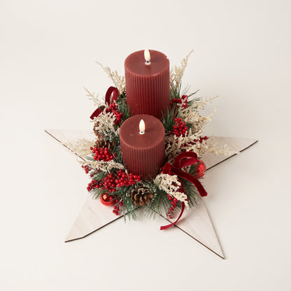 Handcrafted wooden white star candle centerpiece featuring two red pillar candles, natural pinecones, frosted foliage, red decorative balls, and a red velvet bow, against white background