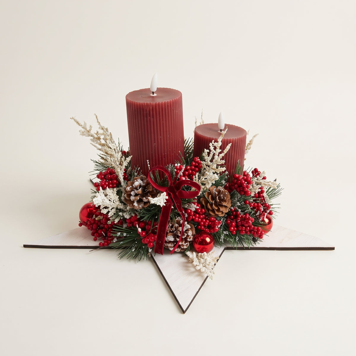 Handcrafted wooden white star candle centerpiece featuring two red pillar candles, natural pinecones, frosted foliage, red decorative balls, and a red velvet bow, against white background