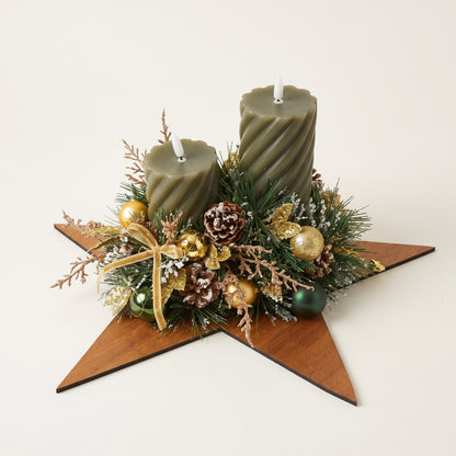 Handcrafted holiday centerpiece featuring two green pillar candles on a wooden star, accented with natural pinecones, frosted foliage, and berries, against white background