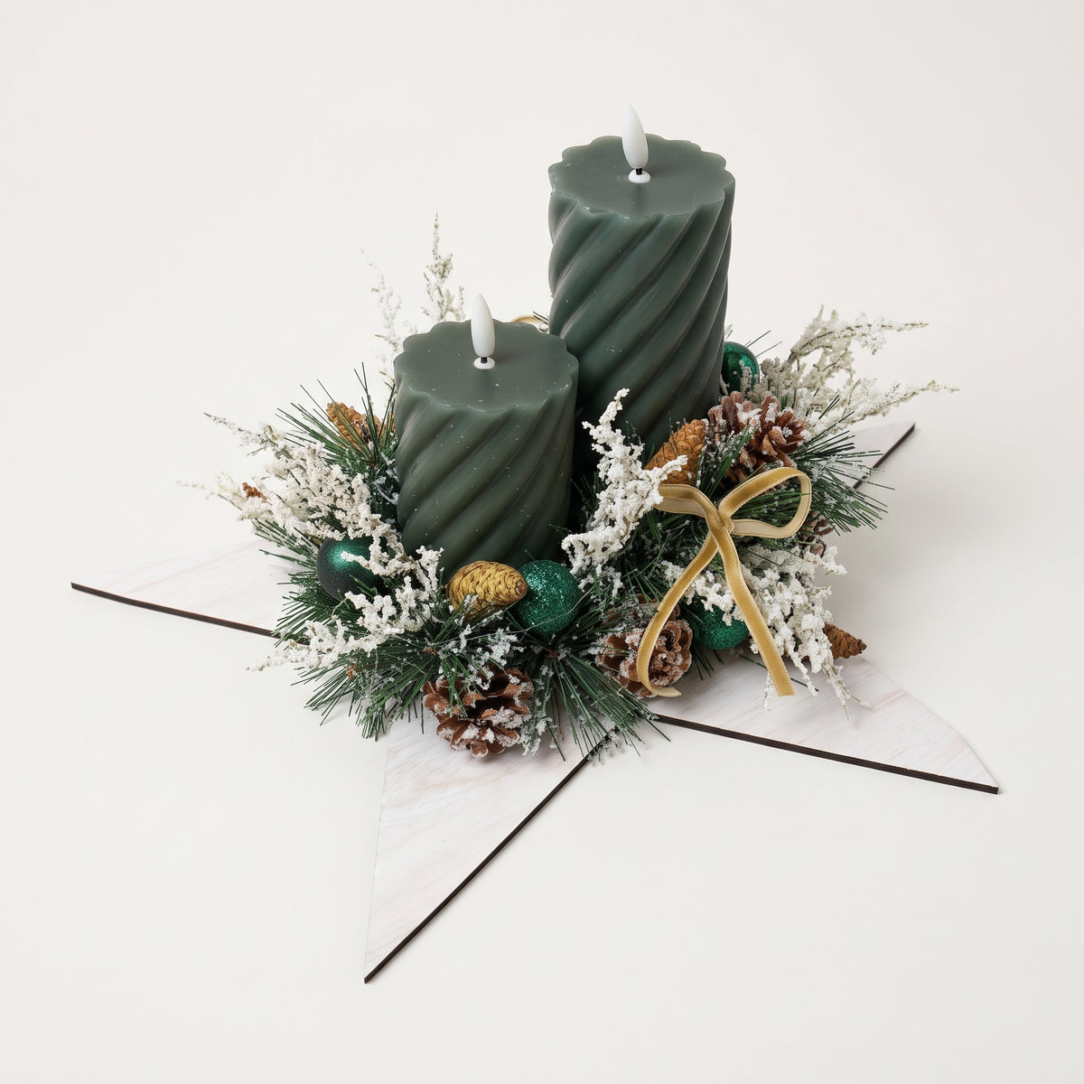 Handcrafted holiday centerpiece featuring two green pillar candles on a white wooden star, accented with natural pinecones, frosted foliage, and berries, against white background