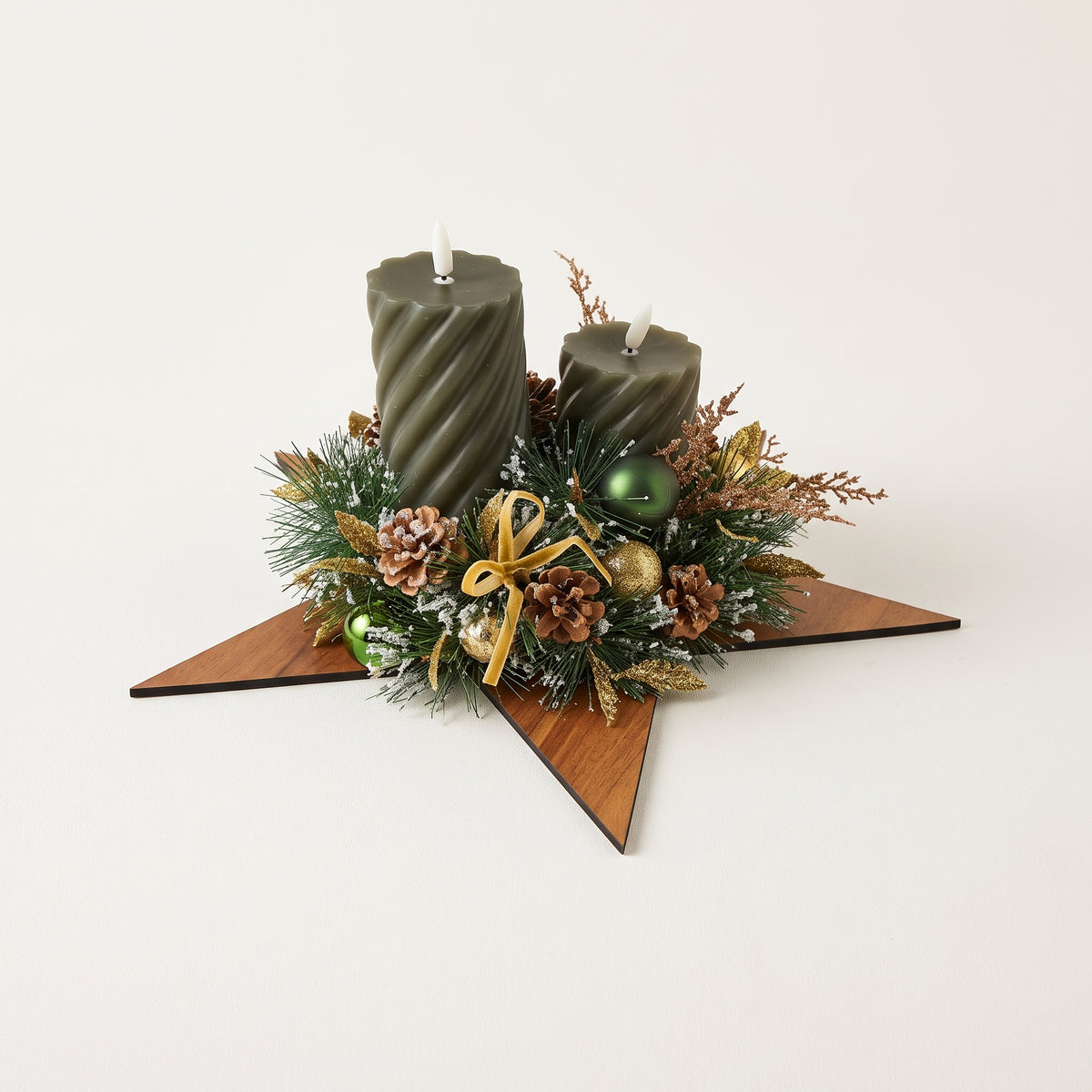 Handcrafted holiday centerpiece featuring two green pillar candles on a wooden star, accented with natural pinecones, frosted foliage, and berries, against white background