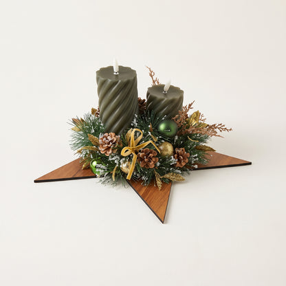 Handcrafted holiday centerpiece featuring two green pillar candles on a wooden star, accented with natural pinecones, frosted foliage, and berries, against white background
