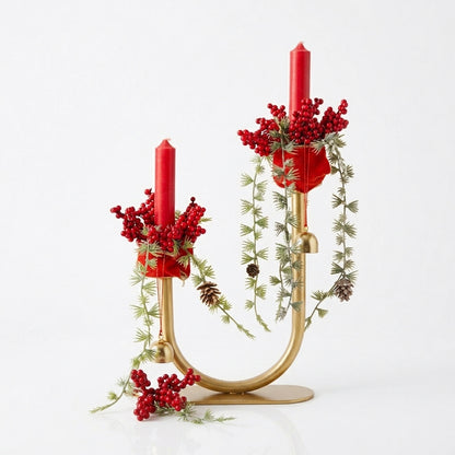 Handmade gold candelabra centerpiece with red pillar candles, evergreen branches, berries, and gold bells for Christmas table decor, designed by Inas.
