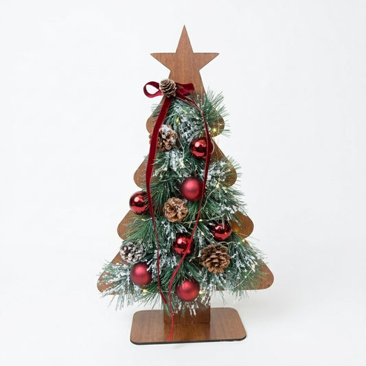 Handmade wooden Christmas tree tabletop decor with pinecones, red ornaments, and snow-dusted pine branches, designed by Inas.