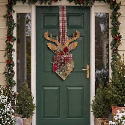 Handcrafted two-sided wooden deer holiday door hanger featuring a festive red plaid tartan ribbon, frosted pine branches, pinecones, berries, and a golden bell, hanging on a classic green front door