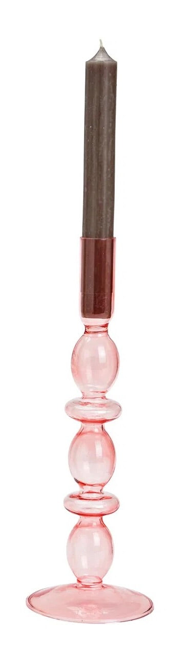 Pink glass candle holder, with a candle lit in the holder. The holder is placed against a white background.