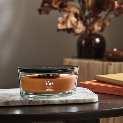 WoodWick Pumpkin Praline candle in a clear glass jar with a black lid, against decorative background