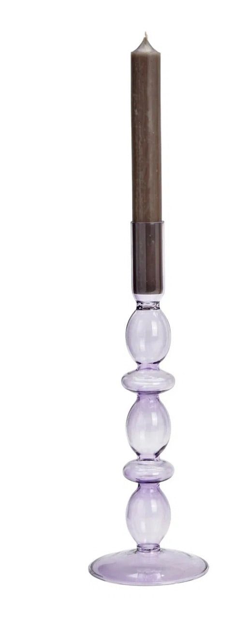 Purple glass candle holder, with a candle lit in the holder. The holder is placed against a white background.
