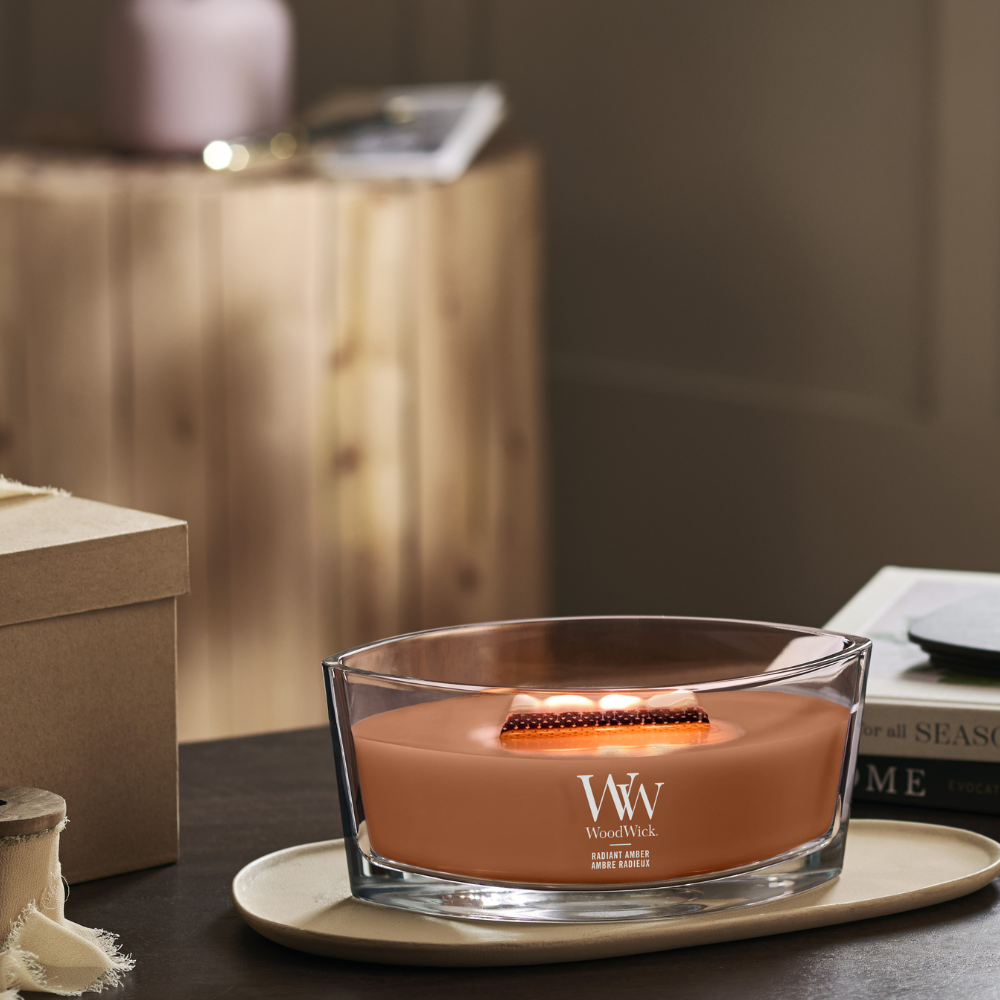 WoodWick Radiant Amber candle in a clear glass jar with an open lid against decorative background