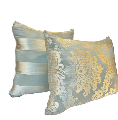Pair of rectangular decorative throw pillows featuring an ornate golden floral damask pattern and soft blue fabric against a white background.