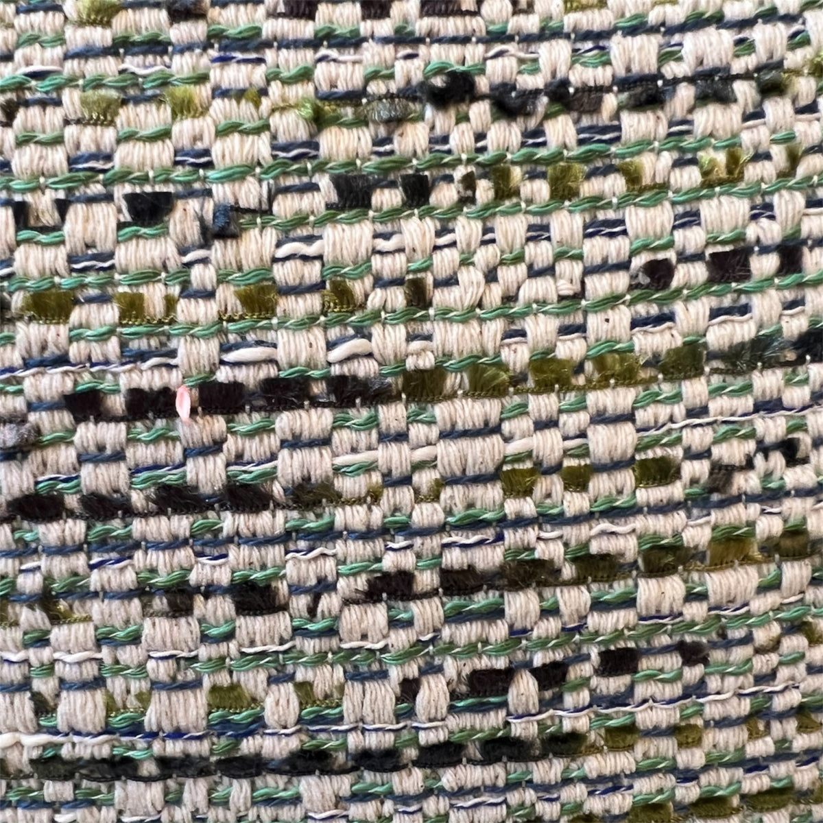 Extreme close-up detail of a textured tweed fabric weave, featuring interconnected threads of sage green, cream, navy blue, and olive green.