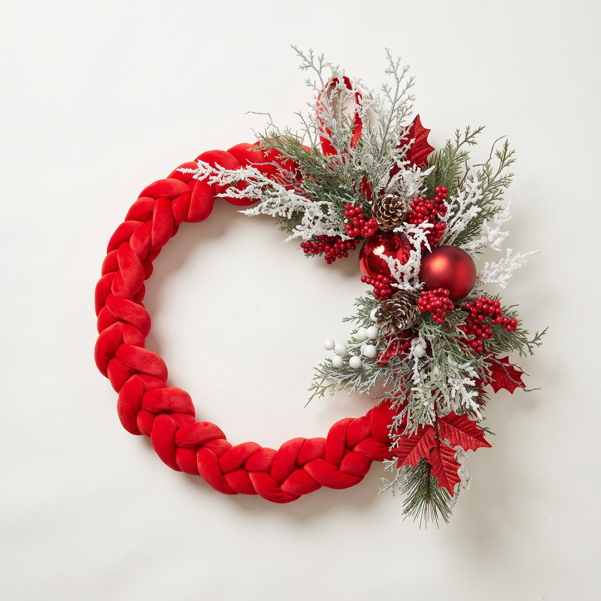 Handmade holiday wreath featuring a red velvet braided loop decorated with red berries, gold leaves, and pine cones, against a white background