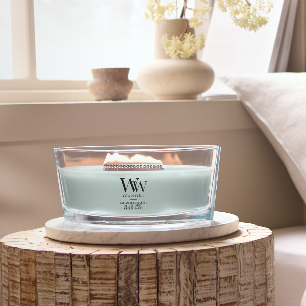 Sage Wood scented candle in a clear glass jar with an open lid against decorative background