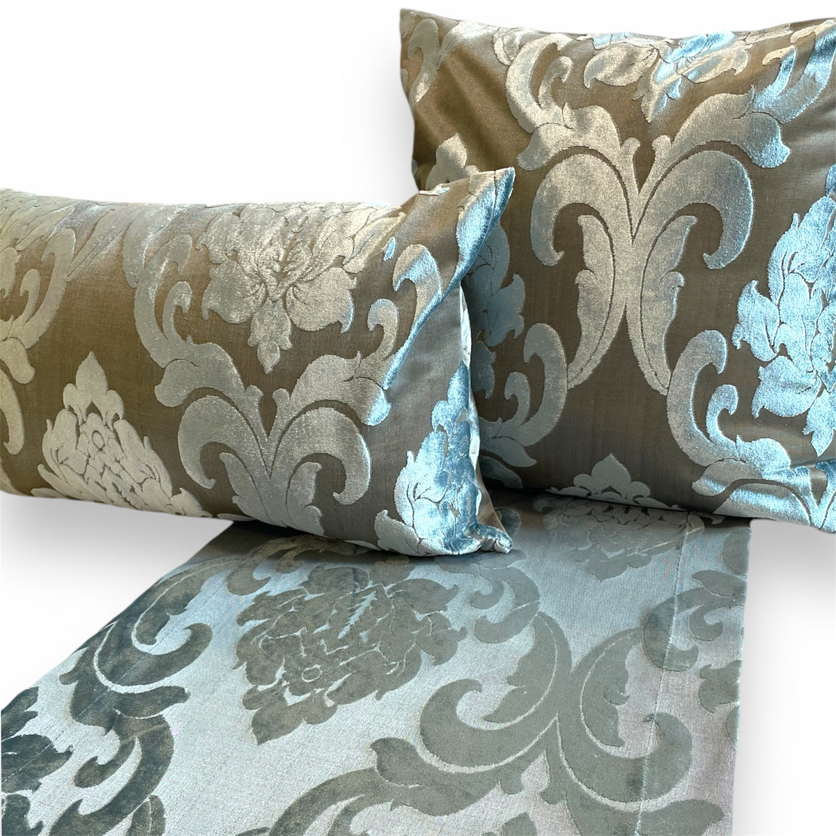 Silver-blue floral damask table runner laid beneath a matching rectangular pillow and large square throw pillow against a white background.