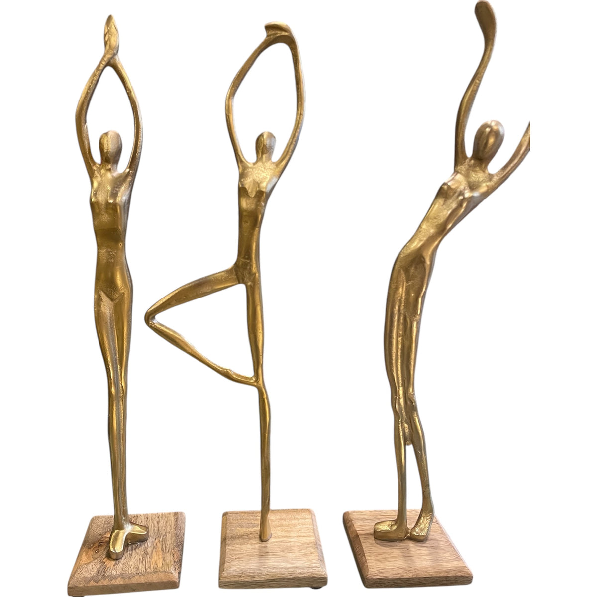 Three Gold metal human stand figures posed on wooden bases, styled on rustic wooden shelves with modern black and white ceramic vases and potted plants.