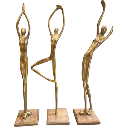 Three Gold metal human stand figures posed on wooden bases, styled on rustic wooden shelves with modern black and white ceramic vases and potted plants.