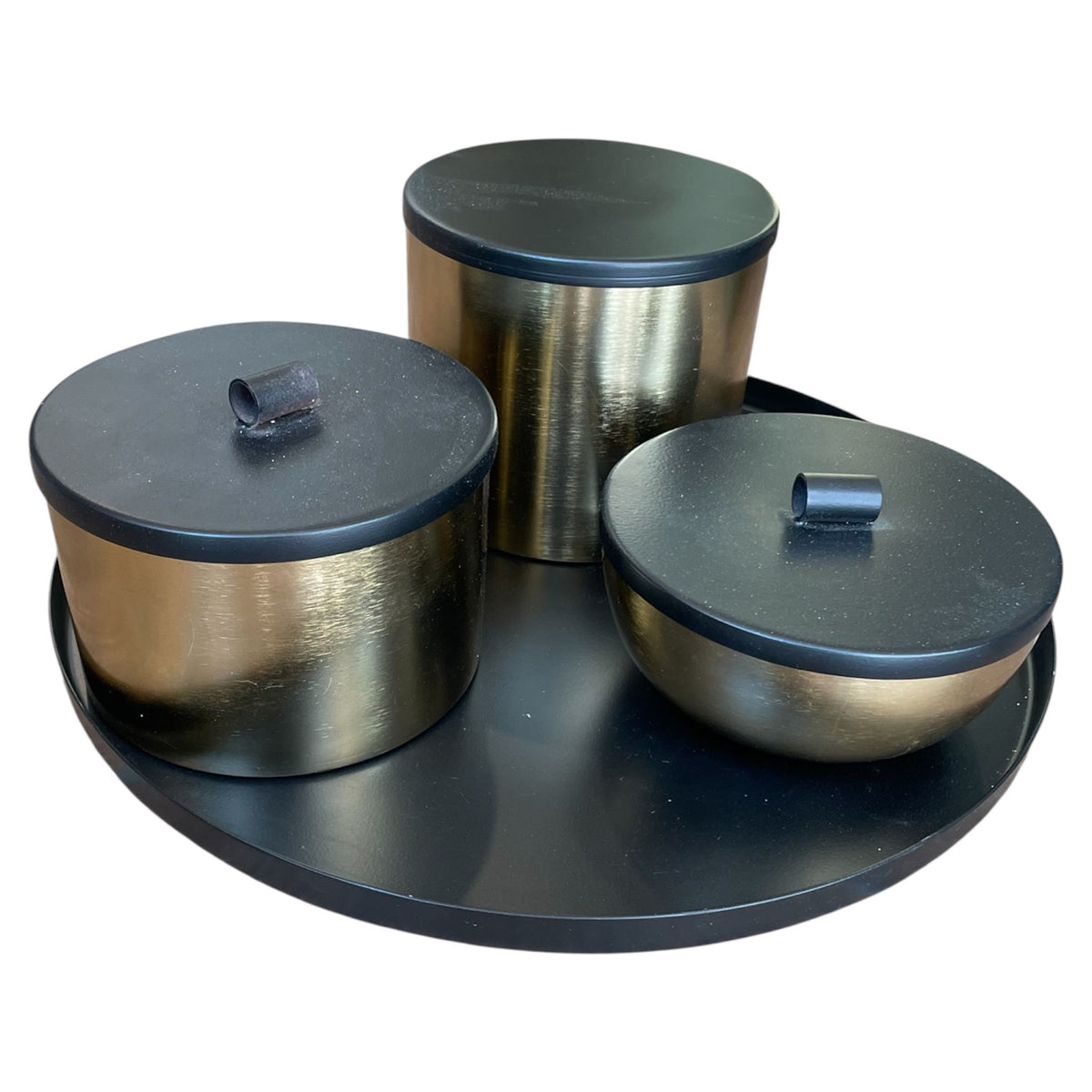 Set of three metallic containers with black lids on a black tray against a white background