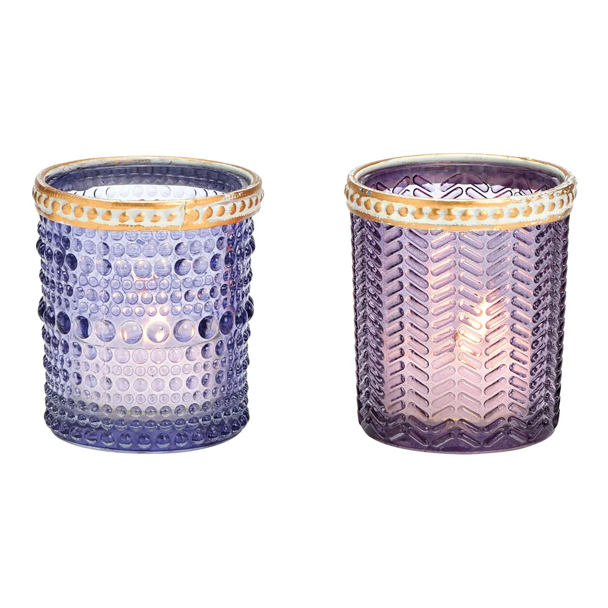Two cylindrical glass candle holders with geometric patterns and brown rims, one with a purple hue and the other with a transparent appearance, both containing lit candles.