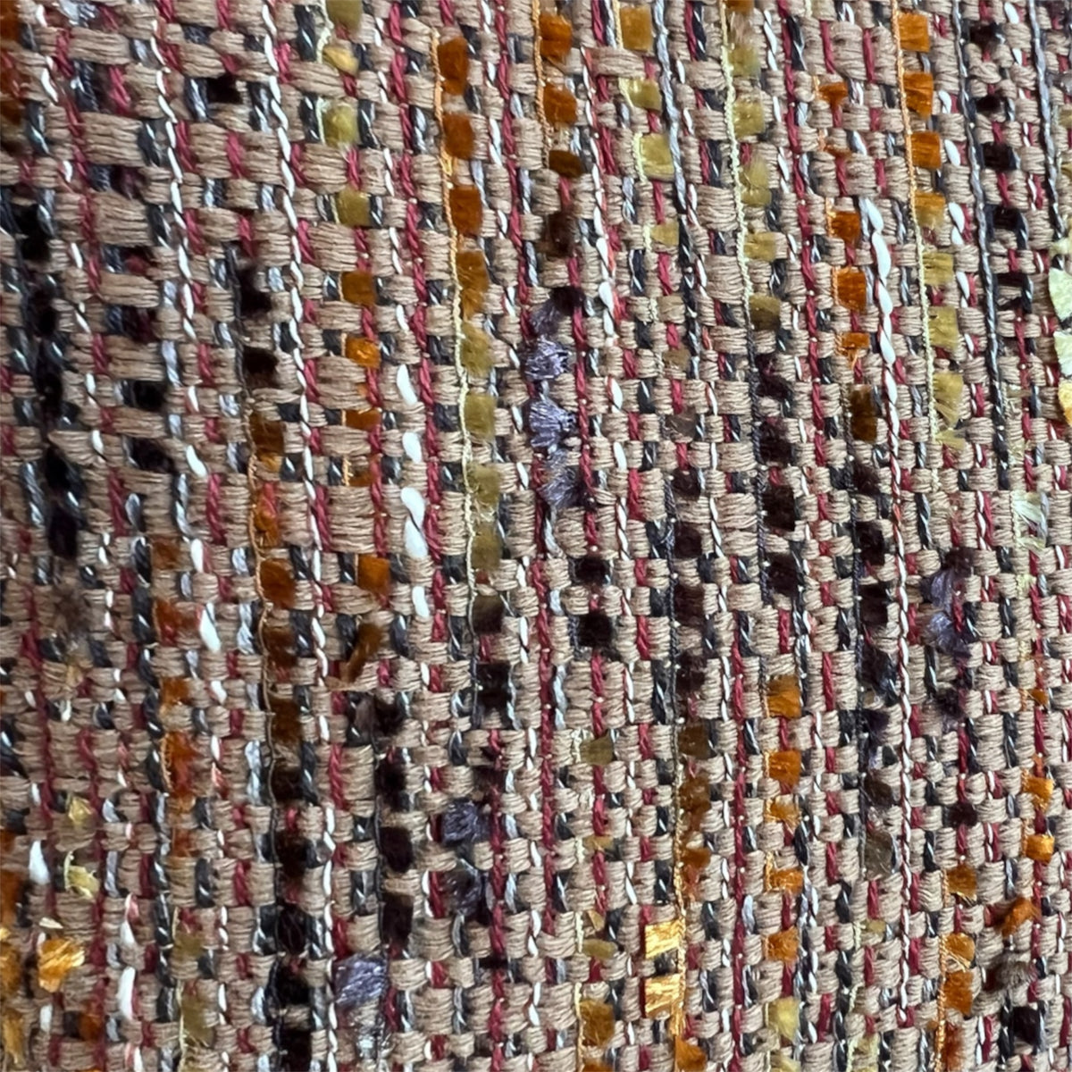 Extreme close-up detail of a rich, multi-colored tweed weave featuring interconnected threads of terracotta orange, ochre yellow, brown, and subtle purple.