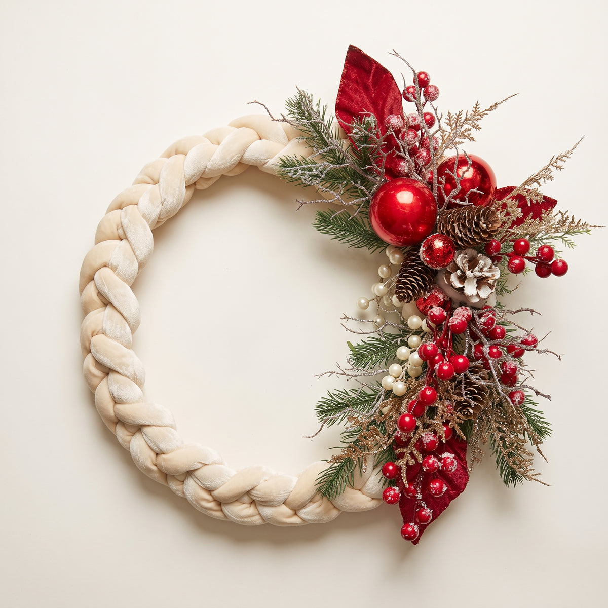 Handmade holiday wreath featuring a white velvet braided loop decorated with red berries, gold leaves, and pine cones, hanging on a rustic wooden door.
