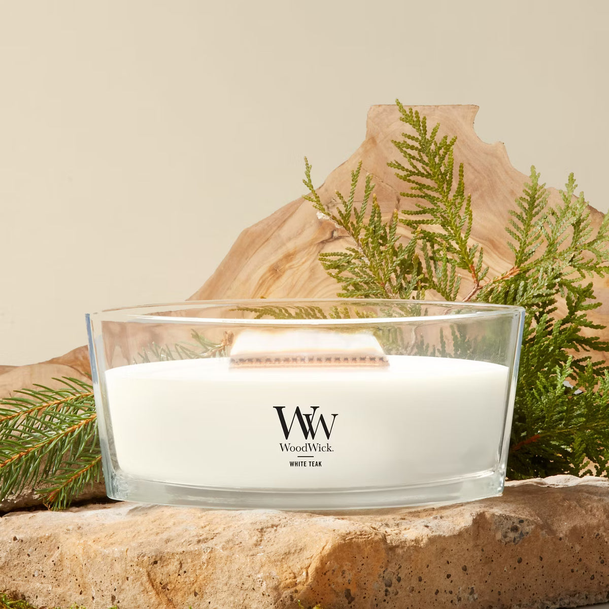 WoodWick White Teak ellipse candle in a clear glass jar with an open lid against natural backround.