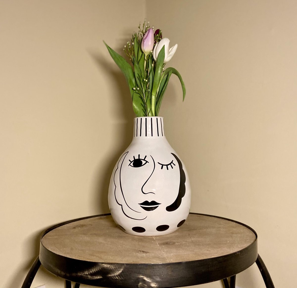 Decorative vase with face design on a wooden stool against a beige wall