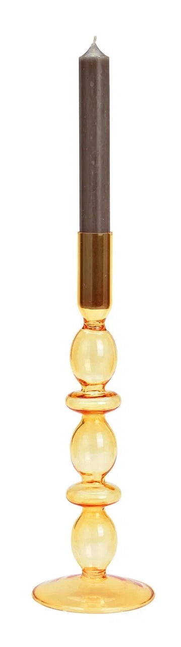 Yellow glass candle holder, with a candle lit in the holder. The holder is placed against a white background.