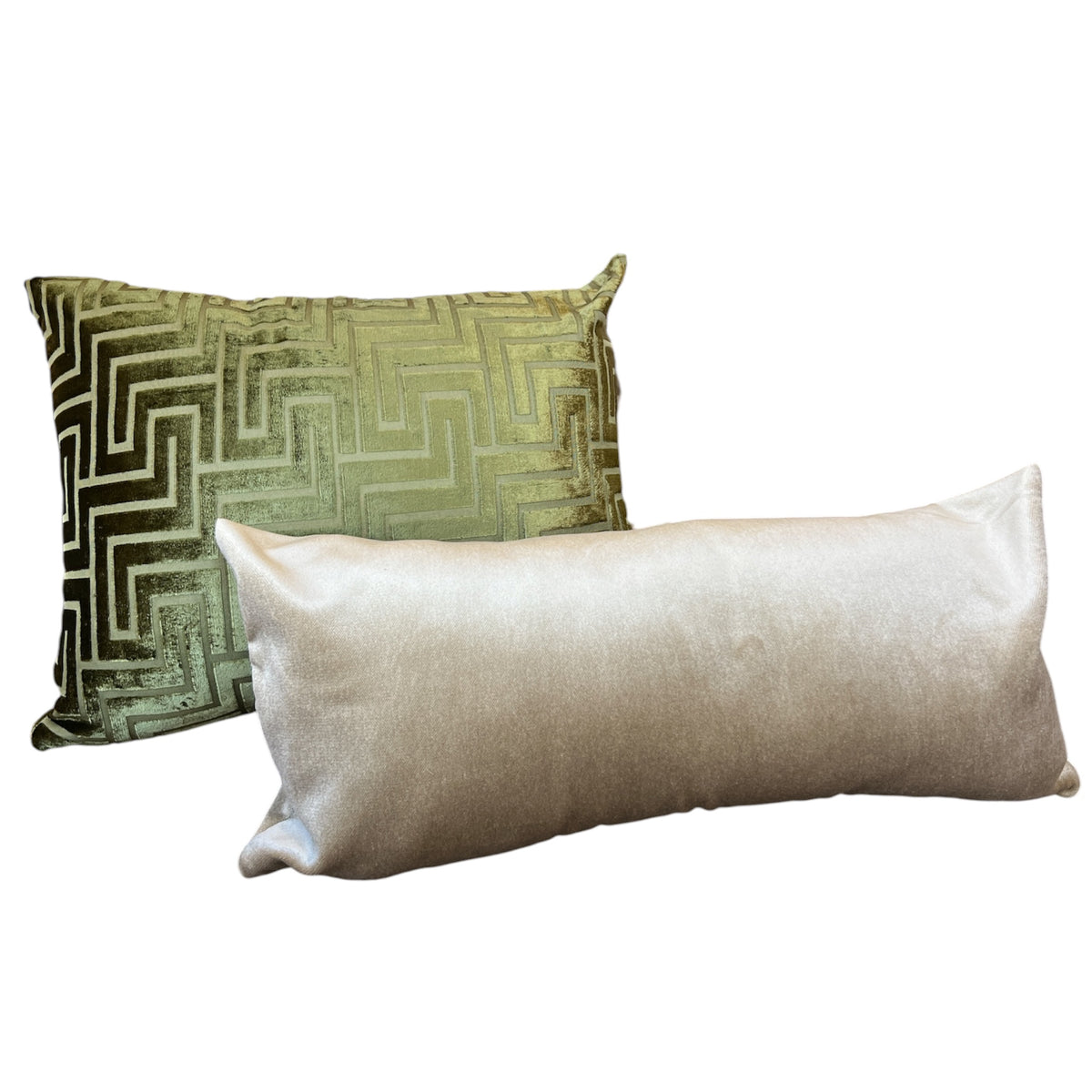 Two decorative throw pillows on a plain white background: a square pillow with a metallic olive-green and gold geometric pattern, and a long rectangular pillow in a light champagne-gold satin fabric.