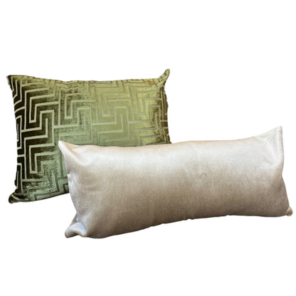 Two decorative throw pillows on a plain white background: a square pillow with a metallic olive-green and gold geometric pattern, and a long rectangular pillow in a light champagne-gold satin fabric.