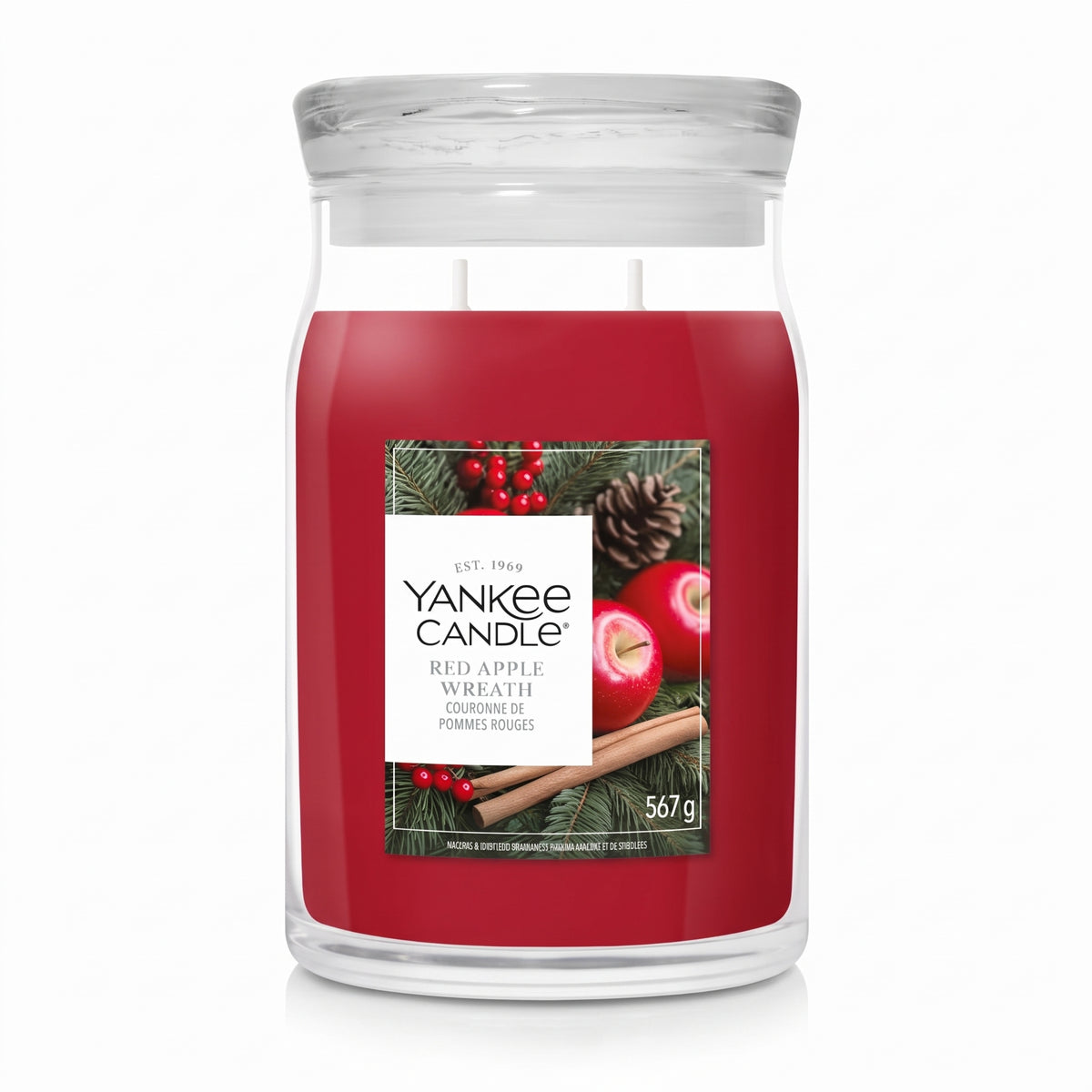 A Yankee Candle jar candle with red wax, a clear glass jar, and a front label featuring red apples, pinecones, and evergreen branches on a white background.